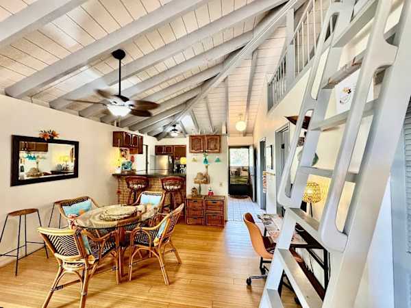 Living room view highlights table, rattan chairs, artwork, and ladder