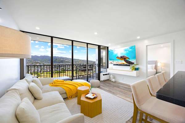 Relax in pure style inside your bright, modern living area, featuring a sectional sofa and floor-to-ceiling glass doors that open up to a private balcony with stunning mountain views.