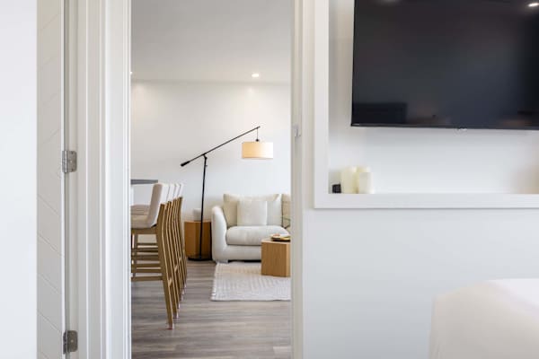 Catch a glimpse of your breezy, open-concept living space, looking through the bedroom doorway into a beautifully lit lounge area complete with warm minimalist decor, comfortable seating, and a stylish breakfast bar.
