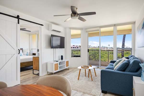 Enjoy a seamless indoor-outdoor feel in your sunlit living area, featuring cozy seating, direct balcony access, and a sliding barn door leading to the bedroom.