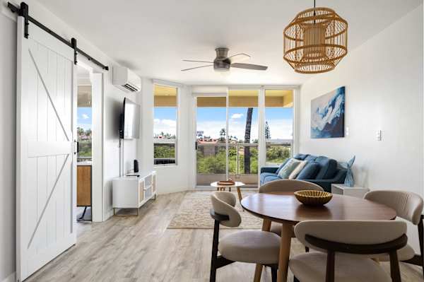 Gather around the table in your airy, open-concept layout featuring a stylish dining nook, charming sliding barn door, and tropical views.