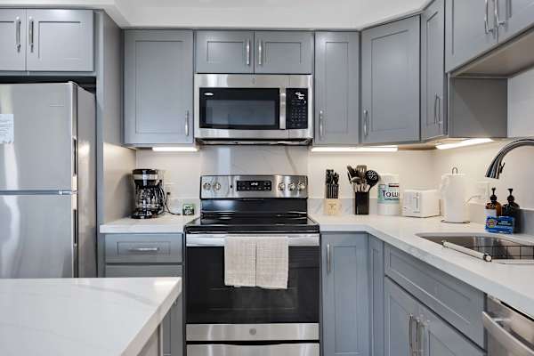 Whip up your favorite meals with ease in this modern, fully equipped kitchen featuring sleek stainless steel appliances, ample counter space, and grey cabinetry.