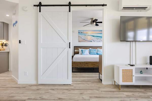 Slide open the chic white barn door to transition seamlessly from the main living area into your private, beach-inspired bedroom retreat.