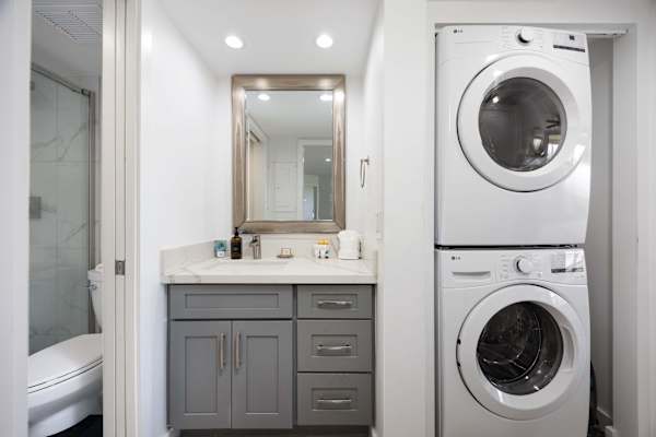 Enjoy maximum convenience with this modern vanity area featuring stylish grey cabinetry, a framed mirror, and a stacked in-unit washer and dryer.
