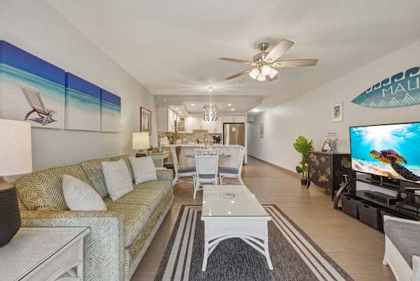 Your spacious open-concept living room seamlessly flows into the dining and kitchen areas, complete with tropical decor, a sleeper sofa, and a large flat-screen TV.