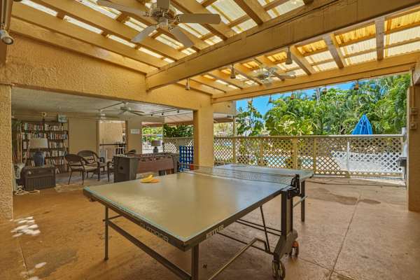 Enjoy open-air table tennis in the covered outdoor recreation space, featuring ceiling fans and views leading out toward the pool area.