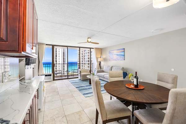 Your beautiful condo features a dining table, a living area with a sofa, kitchen counters, and big glass doors with nice ocean views.