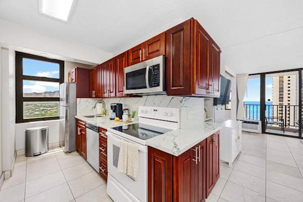 Prepare meals with ease in your well-equipped kitchen featuring rich wood cabinetry, modern appliances, marbled countertops, and views of both the surrounding landscape and the ocean.