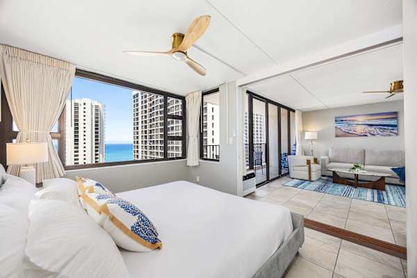 Your bedroom features a king bed, a ceiling fan, a glass window with ocean and city views, and a sliding door that separates it from the living area