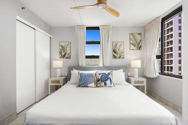 Your cozy bedroom features a comfortable king bed with decorative pillows, nightstands with lamps, a ceiling fan, sliding closet doors, and windows with great views.