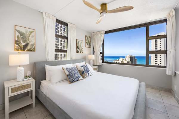 Wake up to ocean views in your serene bedroom, featuring a plush king-size bed, tropical decor, a ceiling fan, and large windows that fill the space with natural light.