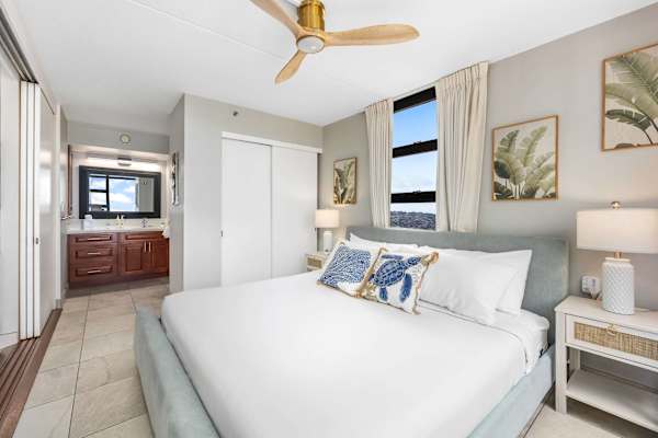 This angle of the bedroom shows your king bed, a ceiling fan, sliding closet doors, and an en-suite view looking into the bathroom area.