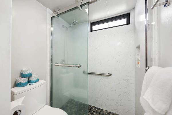 Refresh in your sleek modern bathroom featuring a walk-in shower with sliding glass doors, stone accent flooring, and clean, bright finishes.