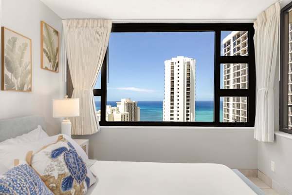 Your bedroom view highlights the large window framing clear views of the ocean, surrounding high-rises, and the bright blue sky.