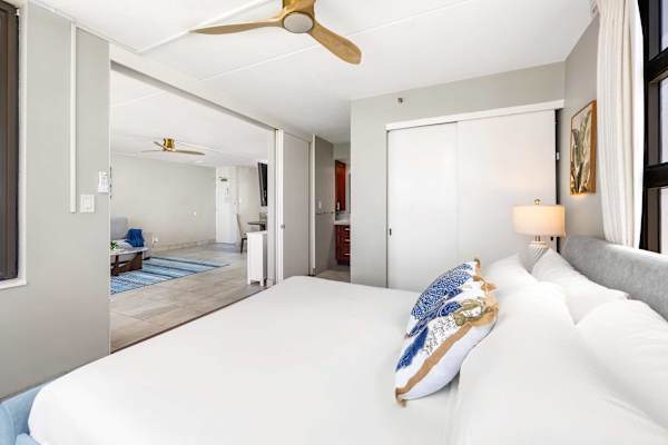 Your king bedroom has a ceiling fan, white closet doors, a lamp on the nightstand, and a sliding door looking into the main living room.