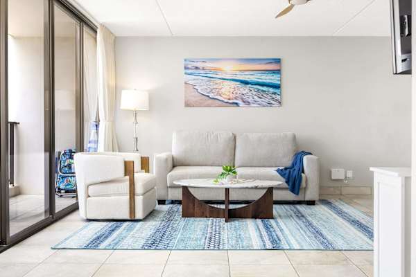 Your living room area features a sleeper sofa, a matching armchair, a coffee table, a blue patterned rug, and large glass doors leading out to the balcony.