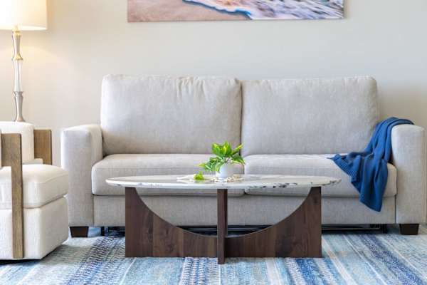 Relax in luxury on your plush, light-grey sleeper sofa paired with a stylish marble-top coffee table and cool coastal accents.