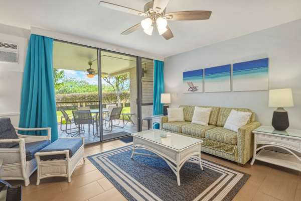 Relax in your bright, beach-inspired living room featuring a sleeper sofa, coastal decor, and large sliding glass doors opening directly onto the private patio.