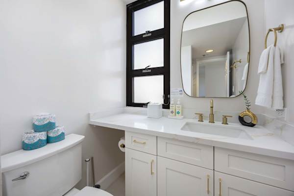 Refresh and unwind in your bright, modern bathroom complete with stylish brass fixtures, a sleek vanity, and a mirror.