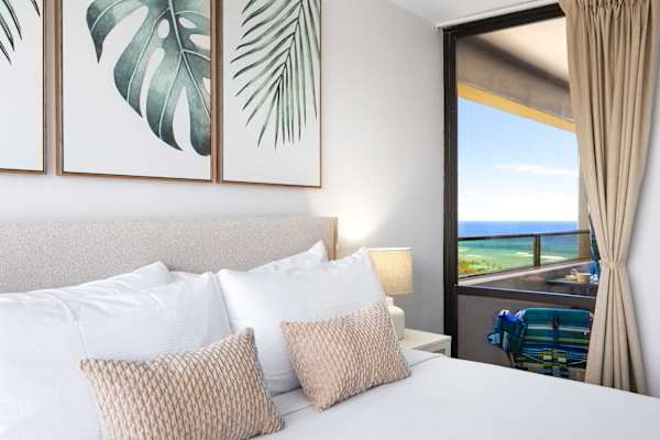 Retreat to your serene, airy bedroom featuring a plush king bed adorned with tropical artwork and direct access to your private balcony.