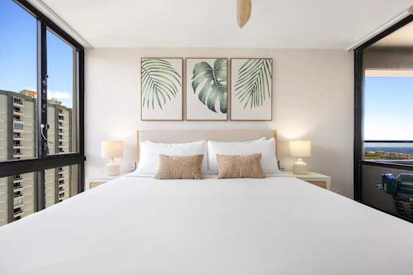 Retreat to your serene, airy bedroom featuring a plush king bed adorned with tropical artwork and direct access to your private balcony.
