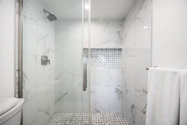 Unwind in your walk-in shower featuring elegant marble-look tiling, stylish accent mosaics, and fresh, plush white towels.