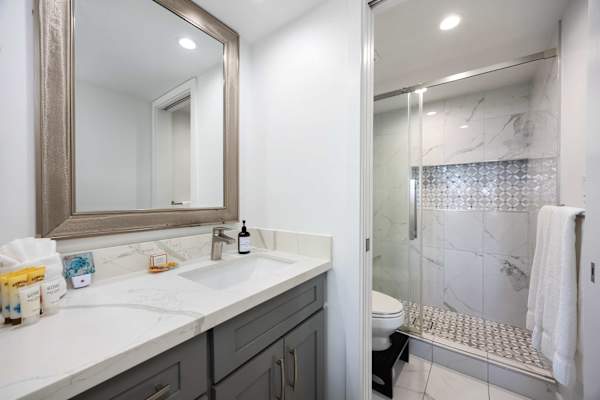 Unwind in your modern bathroom featuring a marble-topped vanity, a large framed mirror, and a walk-in shower with stylish tiled accents.
