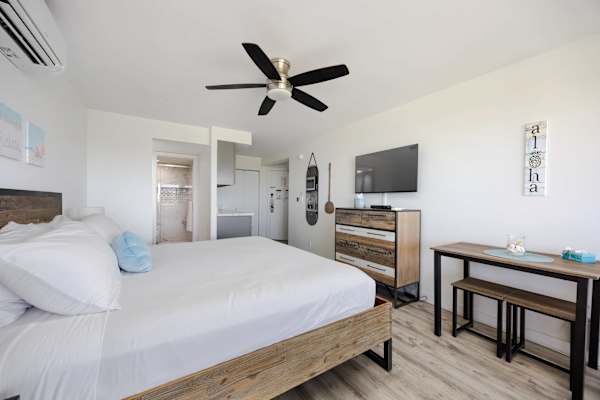 Relax in your stylish studio layout featuring a cozy bed, ceiling fan, TV, dresser, and a dedicated dining table with bench seating.