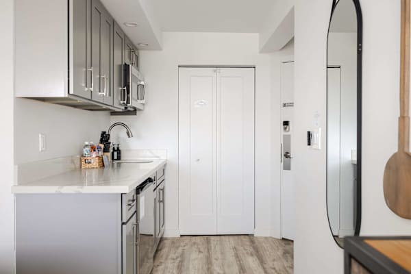 Step into style with your bright, open hallway and modern kitchenette featuring sleek grey cabinets, vinyl flooring, and thoughtful contemporary accents.