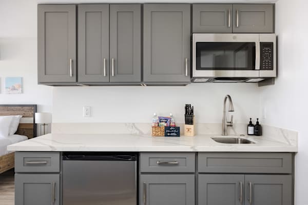 Prepare snacks and light meals with ease using this stylish kitchenette equipped with sleek gray cabinetry, modern stainless-steel appliances, and ample counter space.
