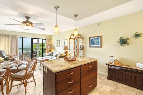 Bask in light-filled, island-style elegance in your open living area featuring a spacious kitchen island, charming dining set, and direct balcony access.