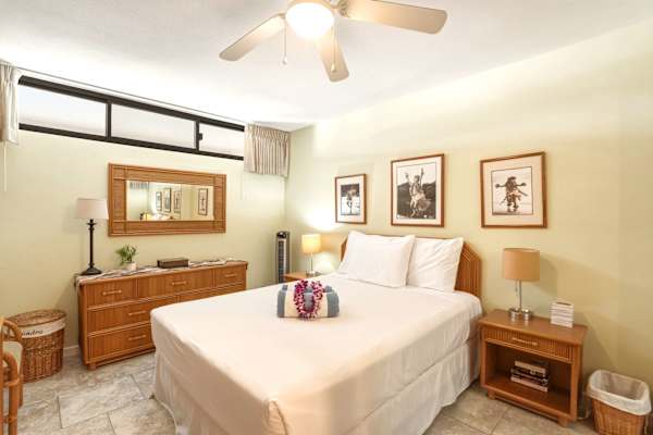 Sleep peacefully in your queen bedroom featuring warm wooden furnishings, soft lighting, ample drawer storage, and a cooling ceiling fan.