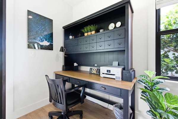 An organized home office workspace features a large dark wooden desk with a hutch