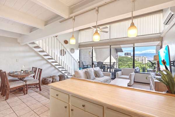 Look out over the open-concept layout from behind the kitchen bar, taking in the inviting dining space, bright living area, and direct access to the scenic balcony.