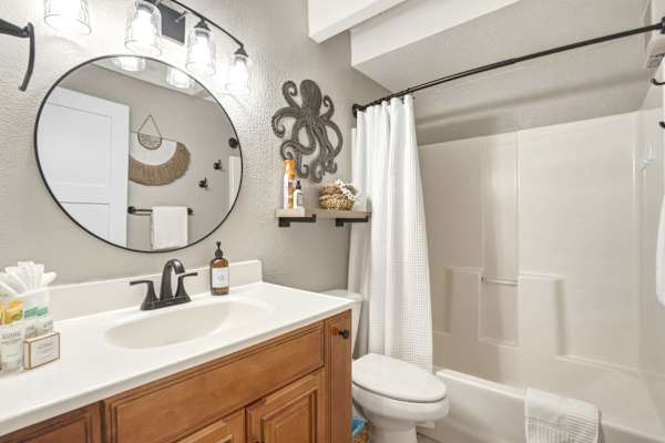 Refresh in your stylish full bathroom featuring a clean vanity, a large round mirror, bright modern lighting, and a soothing shower-tub combination.
