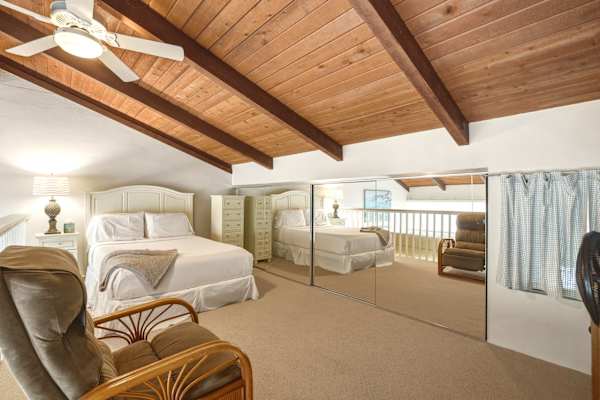 Sleep peacefully in your cozy loft bedroom featuring a plush queen bed, warm wooden vaulted ceilings, mirrored closet doors, and comfortable seating.