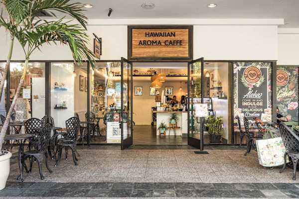 Start your morning with a premium brew at the Hawaiian Aroma Caffe, featuring a chic, open-air storefront and cozy patio seating for the perfect cafe experience.