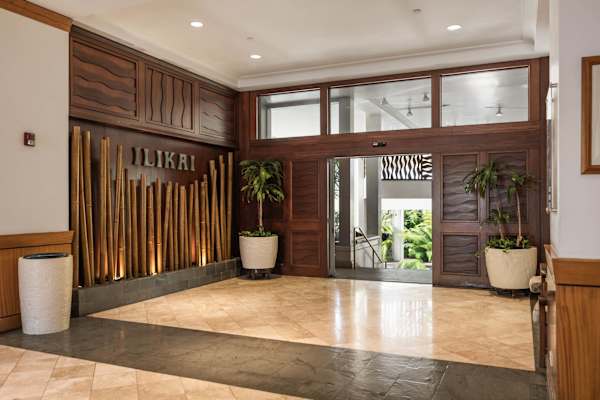 Step inside the warm, sophisticated lobby entryway of the Ilikai, where elegant bamboo accents, rich wood paneling, and polished stone flooring set a welcoming resort tone.