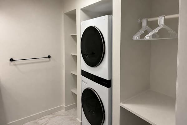 This modern utility area features a stacked washer/dryer integrated into custom white shelving.