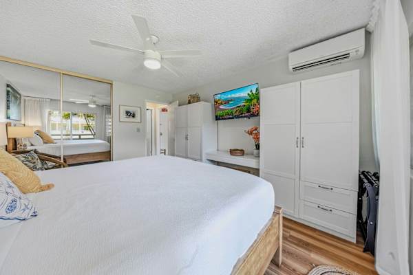 Bedroom view featuring king bed, white wardrobe, split A/C & wall-mounted TV