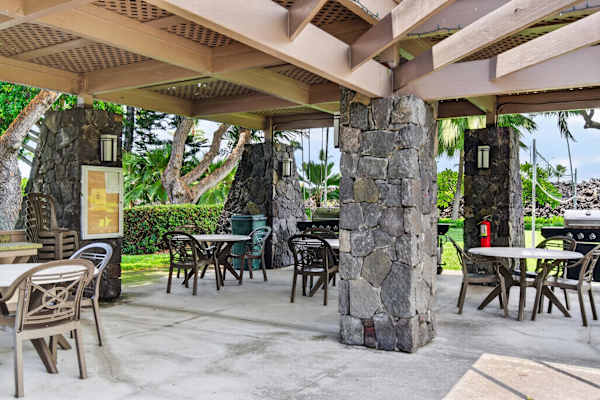 Outdoor covered pavilion with stone pillars, dining tables, and BBQ grills