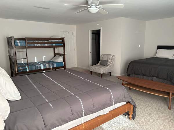 different angle of basement master with king bed, queen bed, and 2 sets of bunk beds, and private bathroom