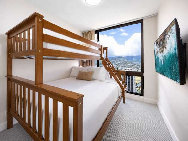 Maximize space and comfort in this cozy second bedroom, featuring a wooden bunk bed w/ queen and twin beds and bright window views.