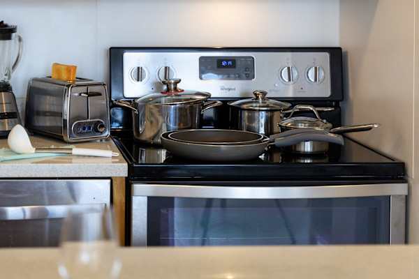 Ready for home-cooked meals, this modern kitchen features a sleek glass-top range complete with quality pots, pans, and cookware essentials.   