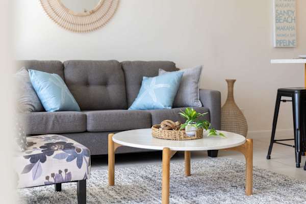 Relax in a stylishly curated living area featuring coastal-hued pillows, a soft textured rug, and a chic round coffee table designed for laid-back comfort.