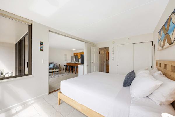 Bright, airy, and inviting, this coastal-style suite features an open-concept layout with white bedding, natural light, and seamless flow into a cozy living area and kitchen.
