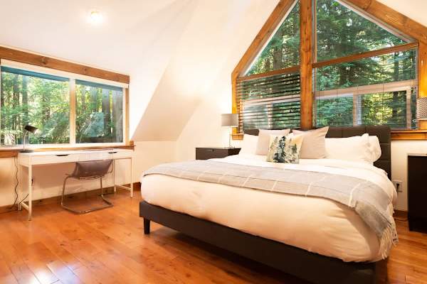 Master bedroom with a comfortable king bed, surrounded by forest drenched windows and a work desk perfect for check ins. 