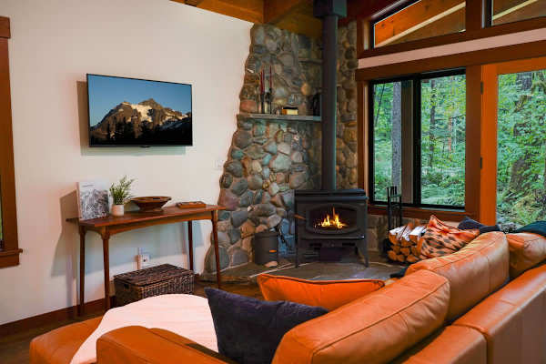 Cozy living room with leather couch, wood burning fireplace with complimentary wood and flat screen TV. 