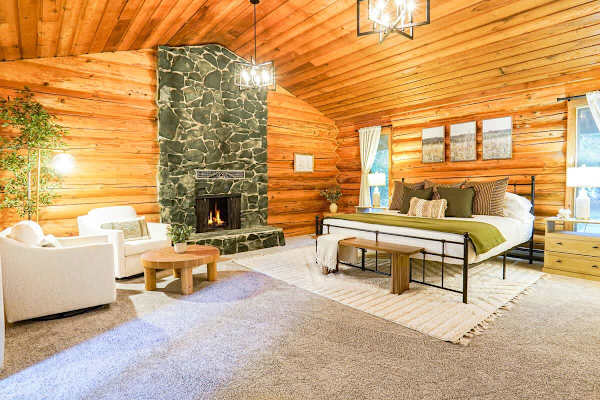 Primary bedroom featuring a Helix king sized bed, cozy seating area, wood burning fireplace, and makeup vanity with mirror. 