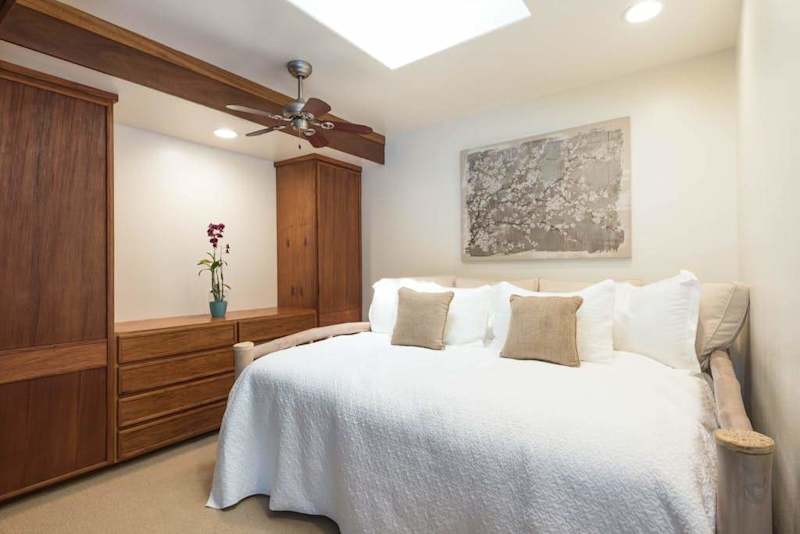 Spacious bedroom combines comfortable bedding, wood accents, and tropical windows